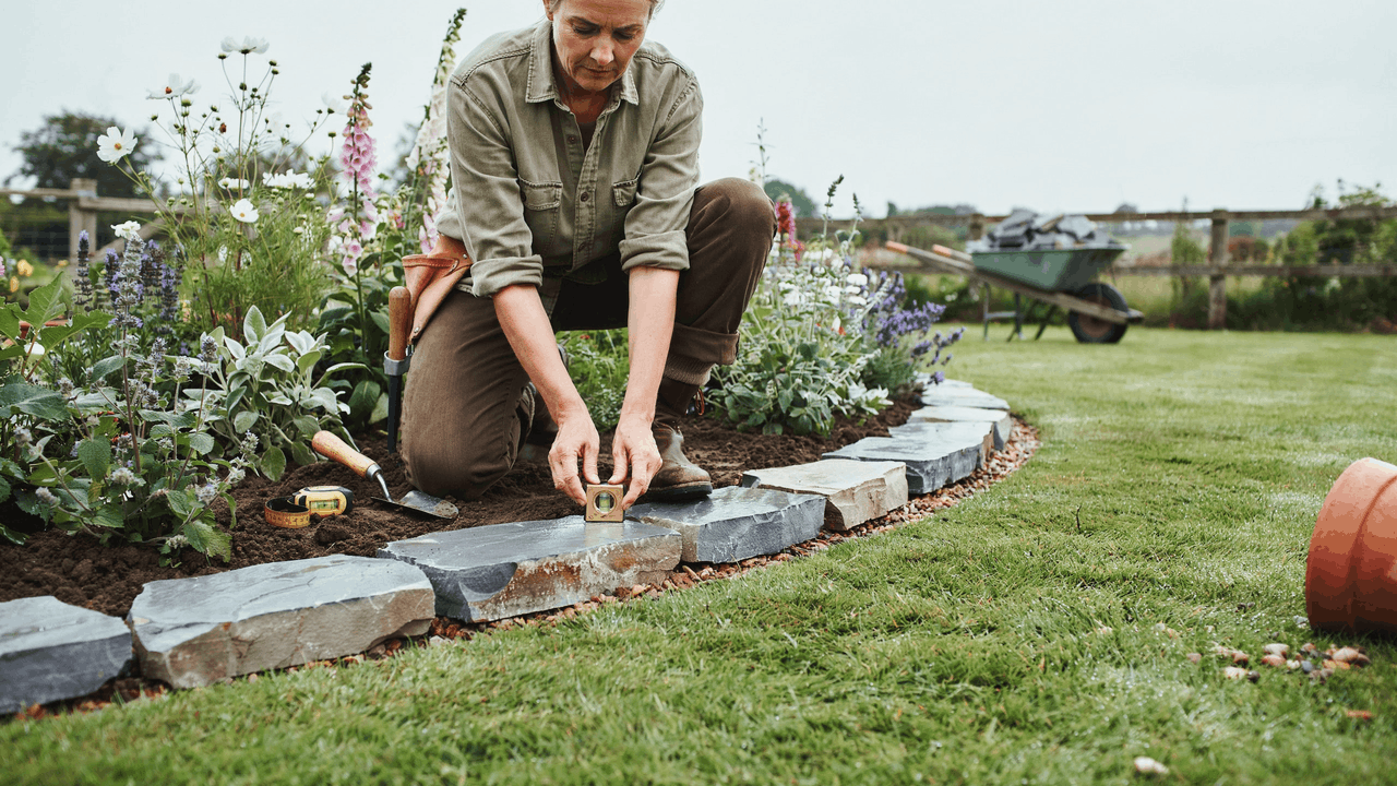 Garden border defined with natural stone edging separating lawn and planting beds in a cottage-style layout.